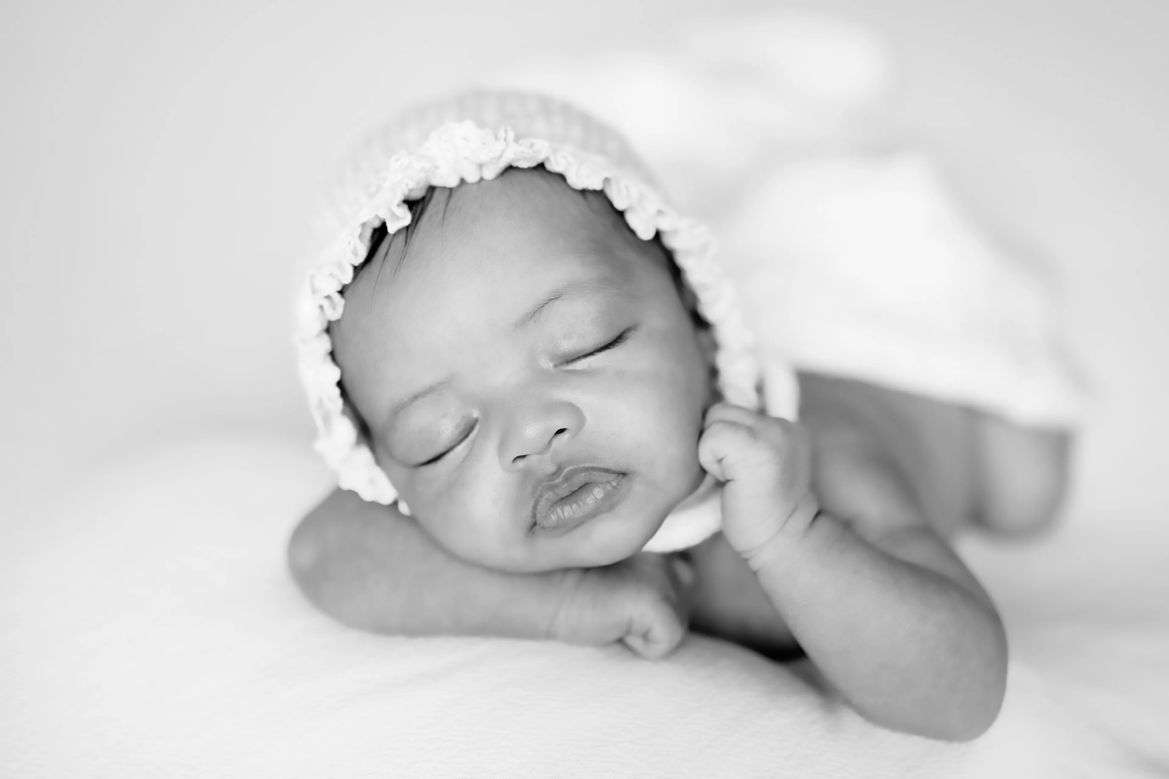 Black-and-white photograph of a newborn asleep in a knit bonnet, wrapped in a soft blanket