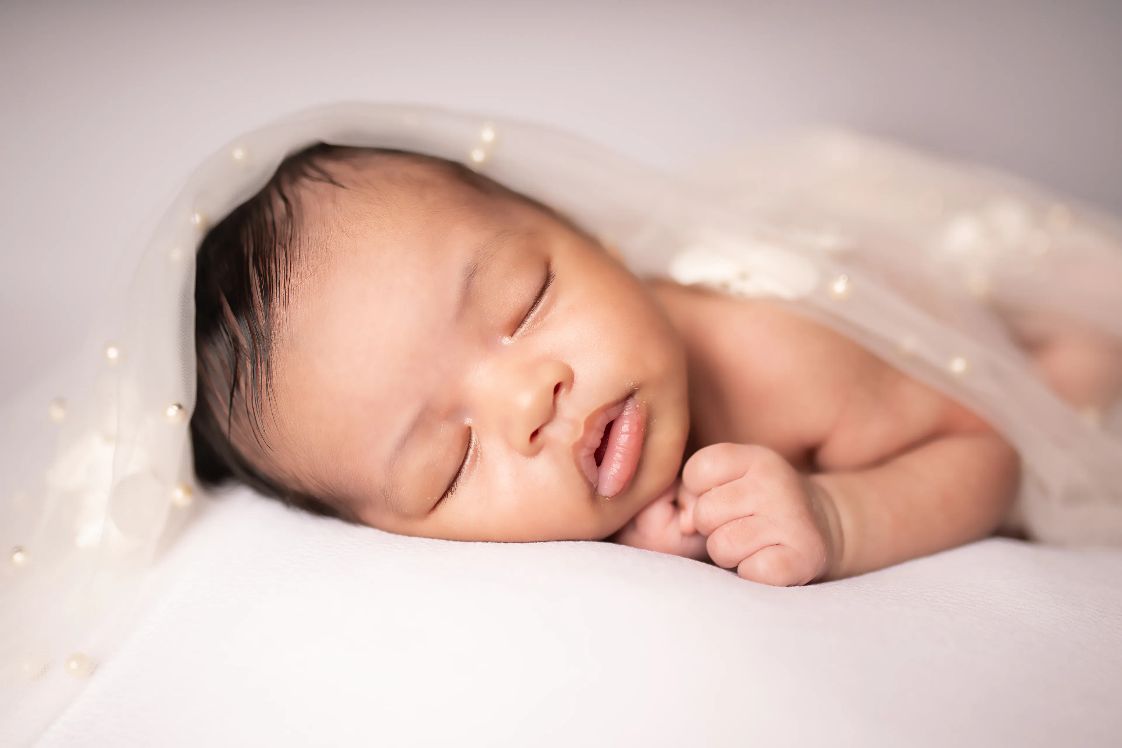 Close portrait of a newborn asleep beneath a sheer veil, her hand curled near her chin