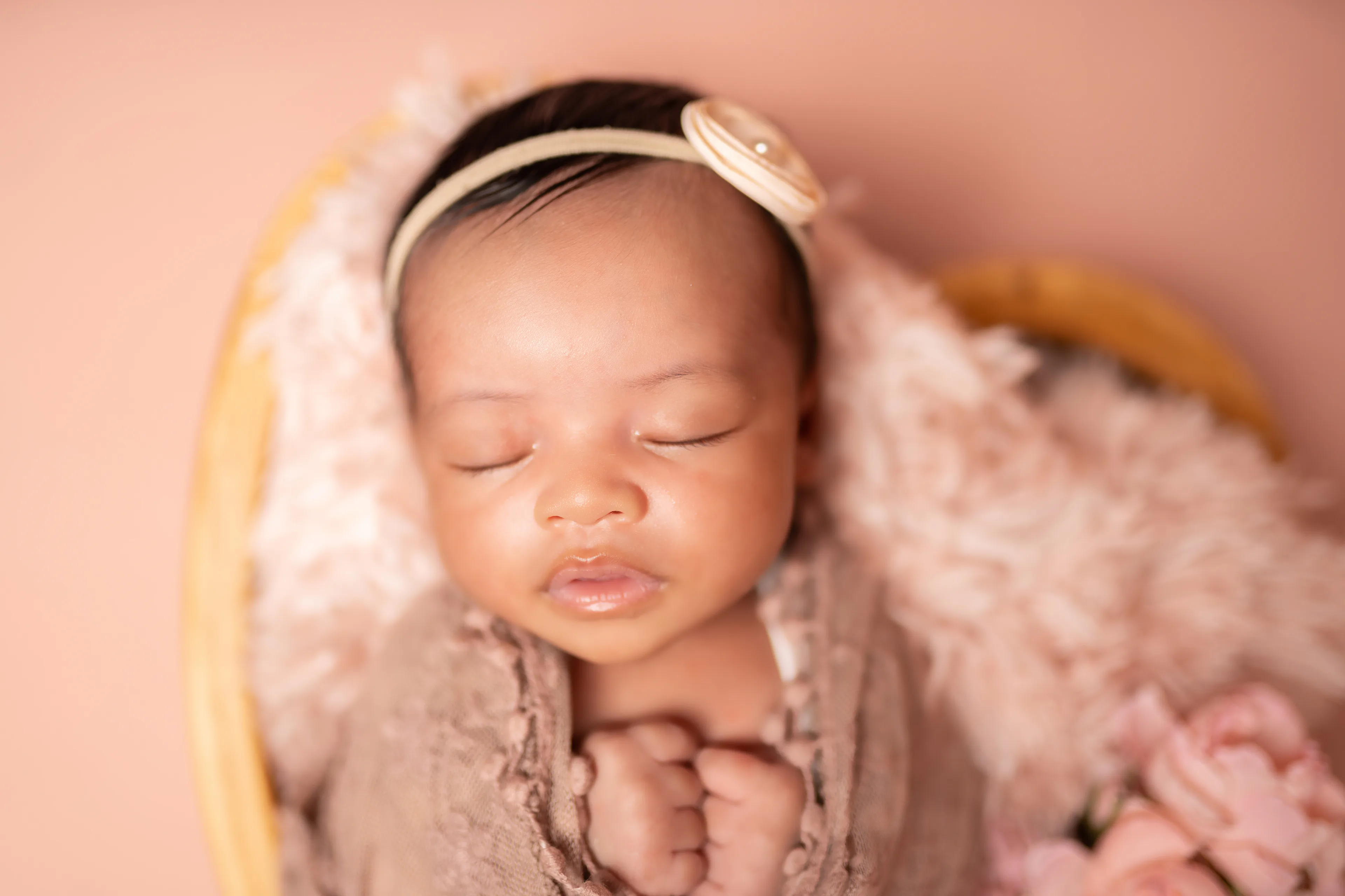 Close view of a newborn asleep in a heart-shaped bowl lined with pink fur, wrapped in brown