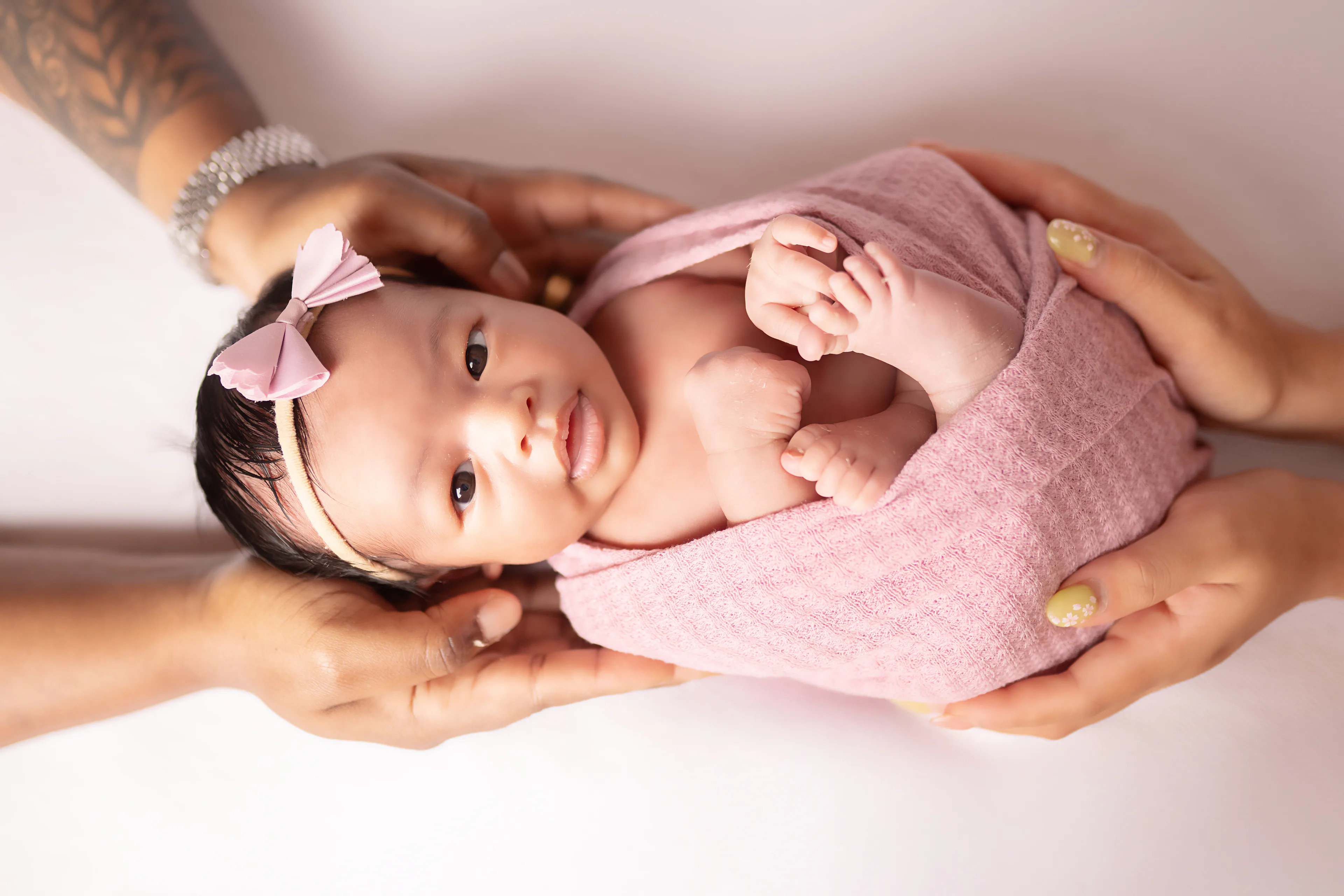 Newborn wrapped in pink, held in two hands, her eyes open