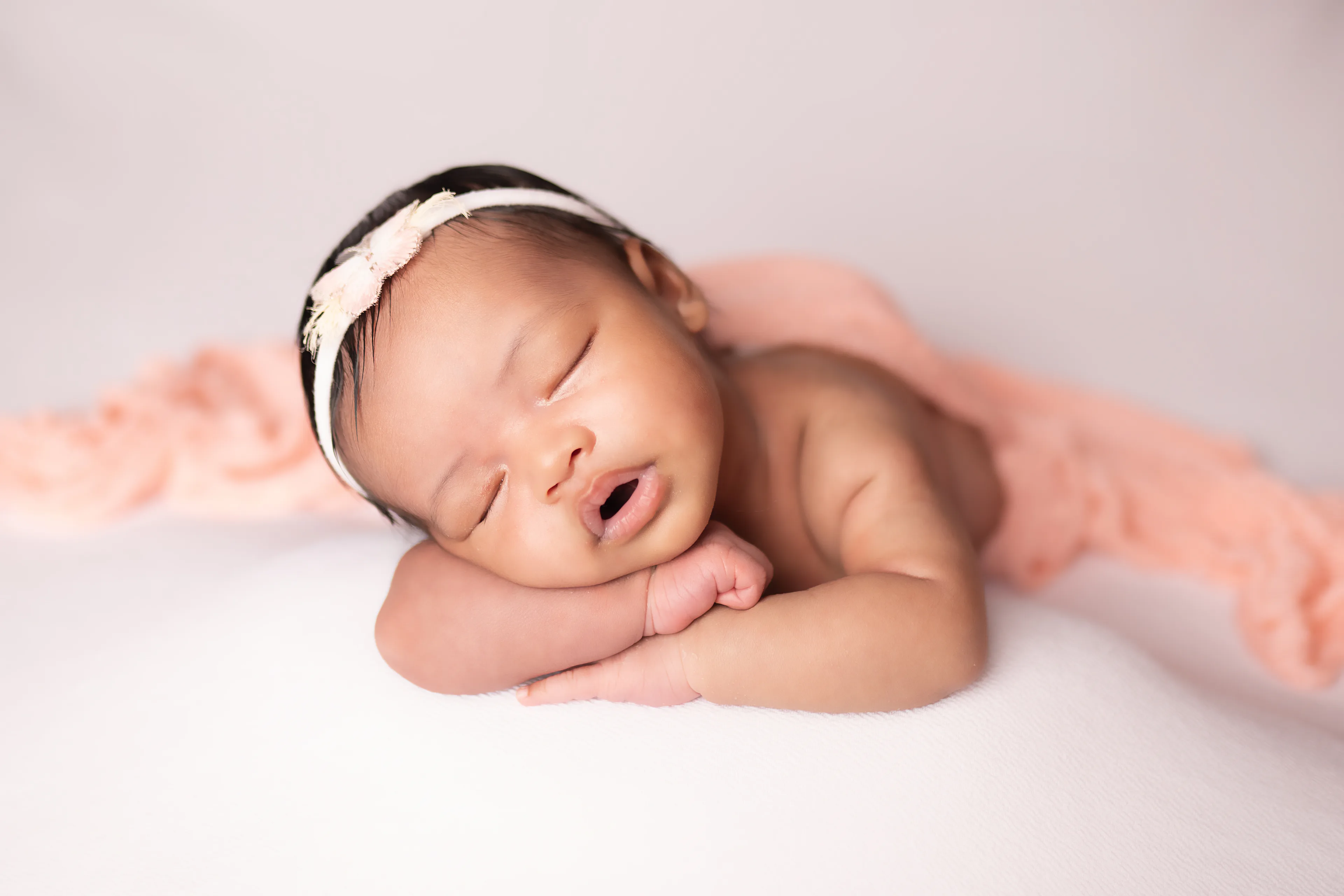 Newborn asleep with her cheek on her folded arms, a pink wrap draped over her back