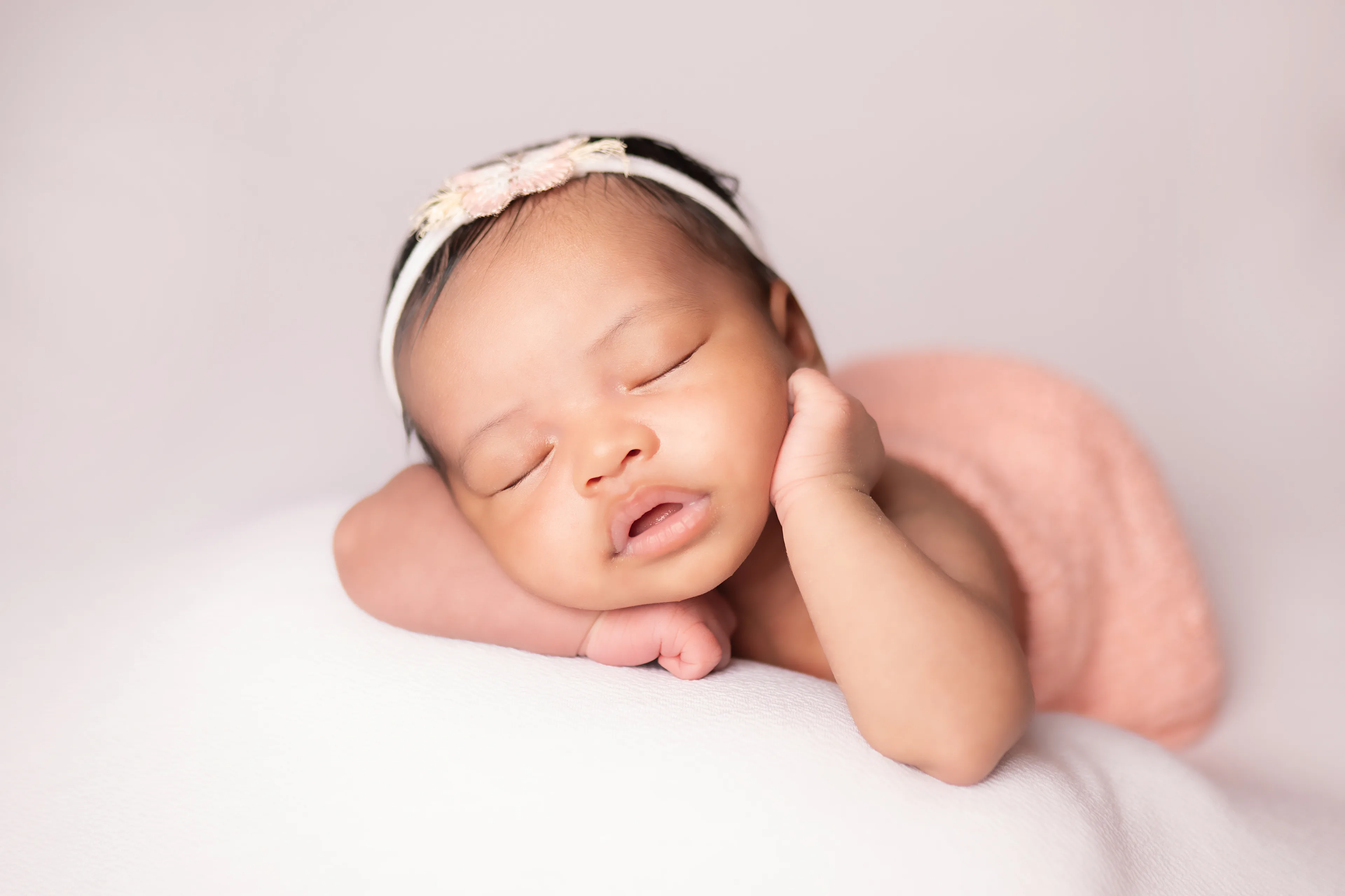 Newborn asleep on her side with a pink wrap, one hand raised near her face